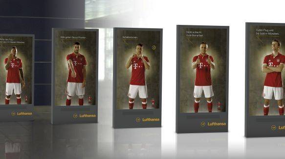 Spieler des FC Bayern führen für die Lufthansa am Flughafen München auf Videoscreens Übungen vor.