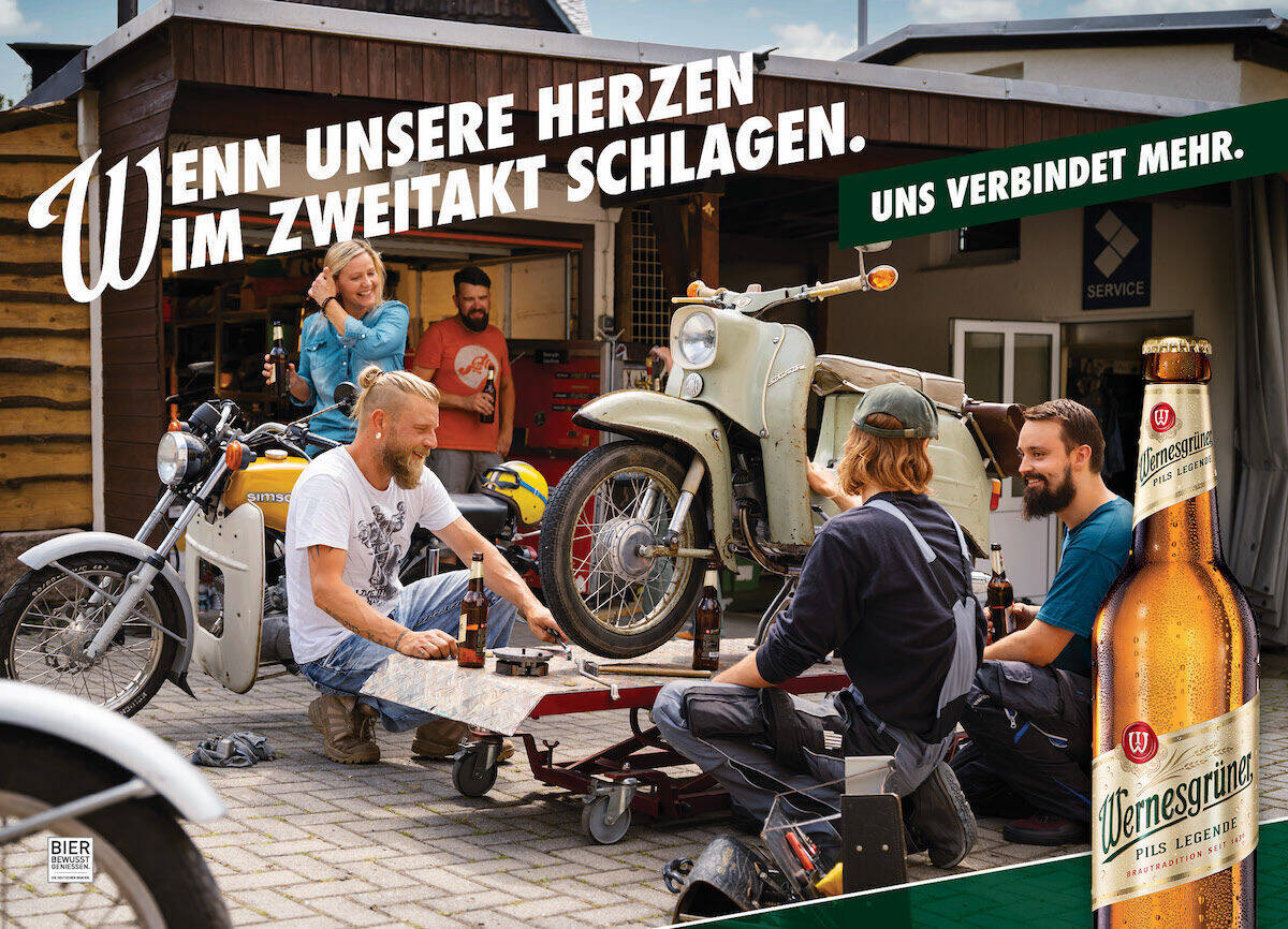 Junge Männer schrauben an einem Motorrad, währenddessen trinken sie Wernesgrüner Bier.