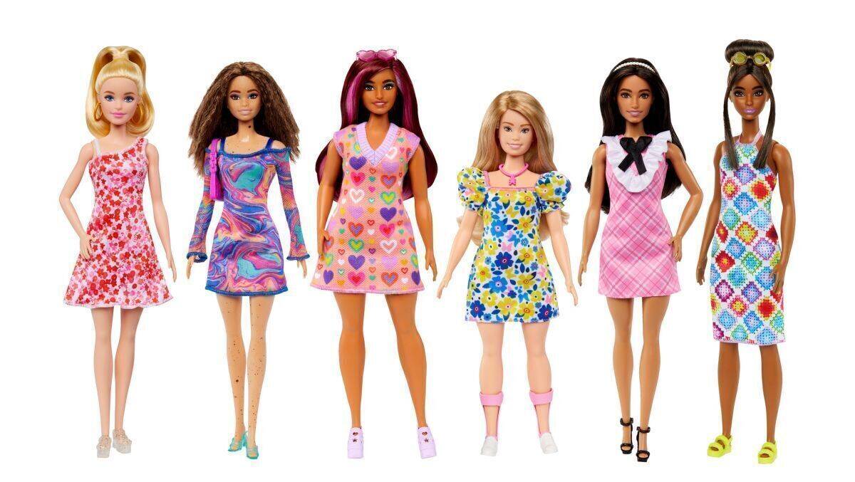 Die Barbie im Blümchenkleid hat das Downsyndrom. Sie trägt rosafarbene Orthesen und Turnschuhe mit Zipper. 