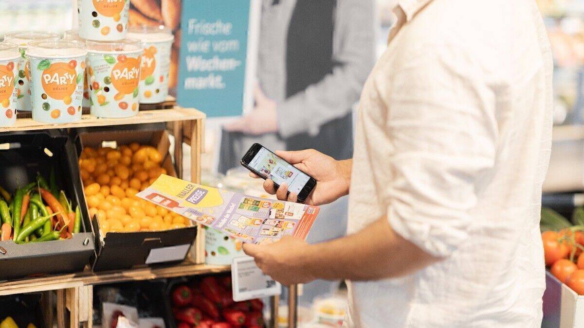 Ein Kunde schaut auf einen Prospekt - sowohl analog als auch digital. Bei Rewe wird es bald nur noch die zweite Variante geben.