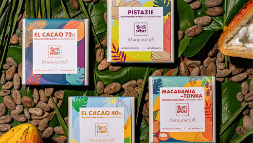 Die vier neuen Manufaktur-Schokoladen von Ritter Sport vor einem Hintergrund von Blättern und Kakaobohnen